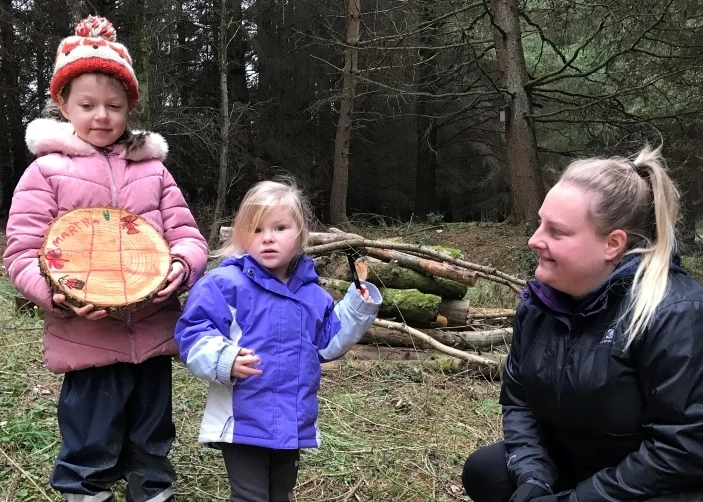 An adult with two small children making crafts from wood